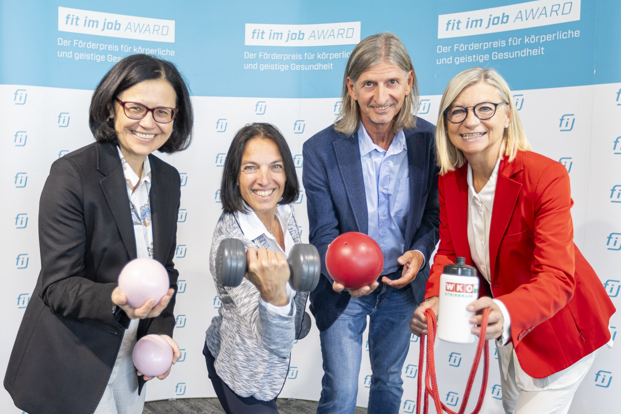 Sandra Holasek, Beatrice Erker, Franz Endthaller und Daniela Gmeinbauer mit Bällen, Hantel, Springseil und Trinkflasche vor der Fotowand des fit im job Award